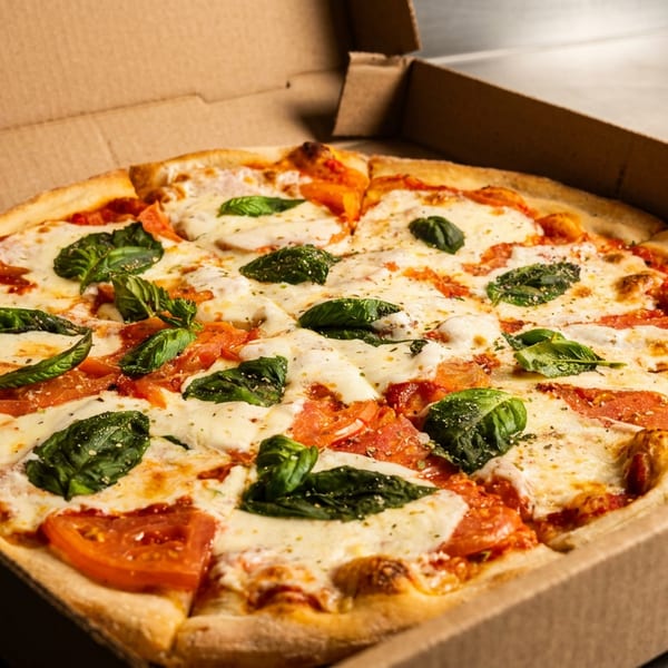 Freshly baked Margherita pizza with basil, mozzarella, and tomato in a cardboard delivery box.