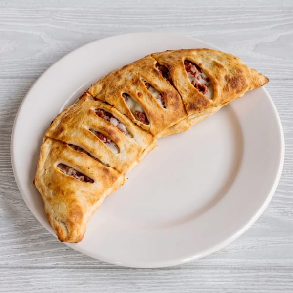 A golden-brown calzone with visible cheese and meat filling, served on a white plate.
