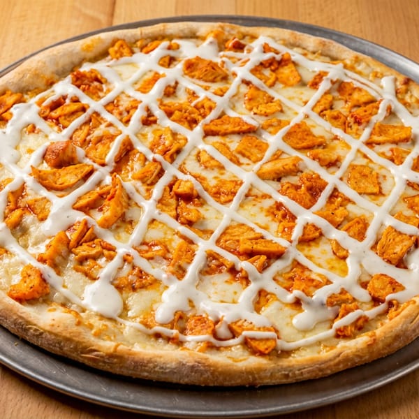 Buffalo chicken pizza with white sauce drizzled in a lattice pattern on a metal tray.