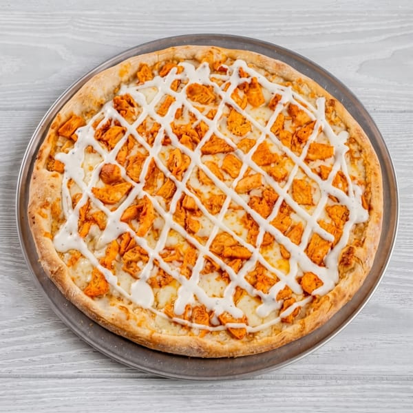 Buffalo chicken pizza with ranch dressing drizzled in a lattice pattern on a metal tray.