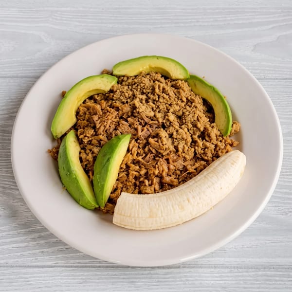 Savory ground meat with avocado slices and a peeled banana on a white plate.
